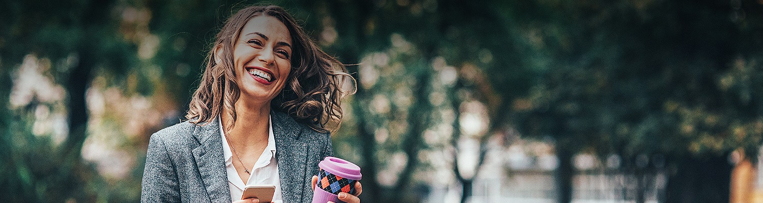 business woman walking down the street holding her phone and coffee cup