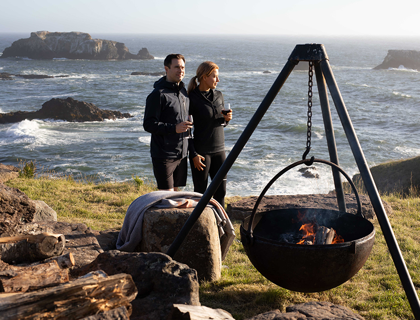 two people drinking wine next to the bluff with a fire pit