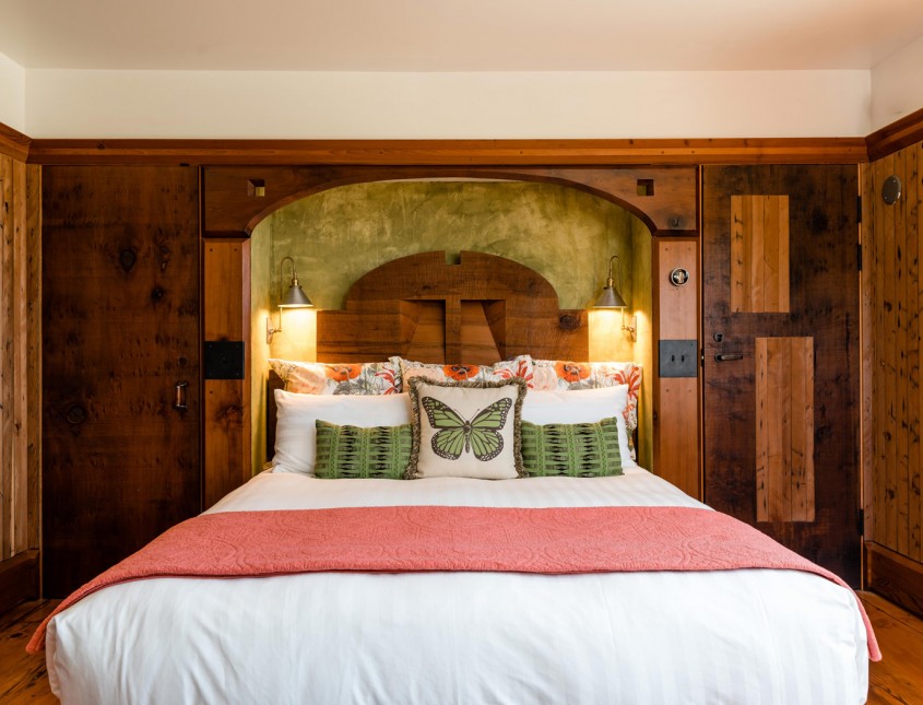 guest bed with white linens, pink blanket, green pillows, and wooden walls