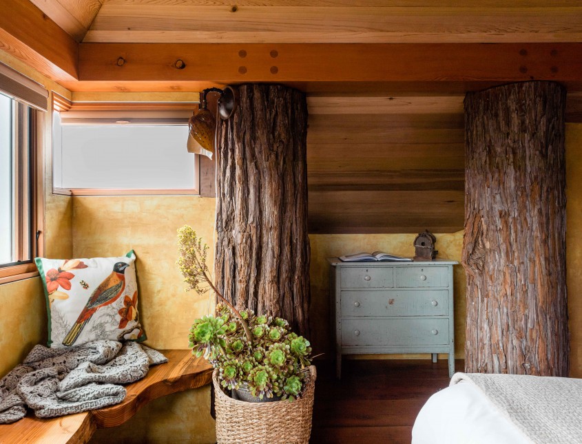 interior of a guest room with two wooden logs built into wall with dresser in between and a wooden bench by window