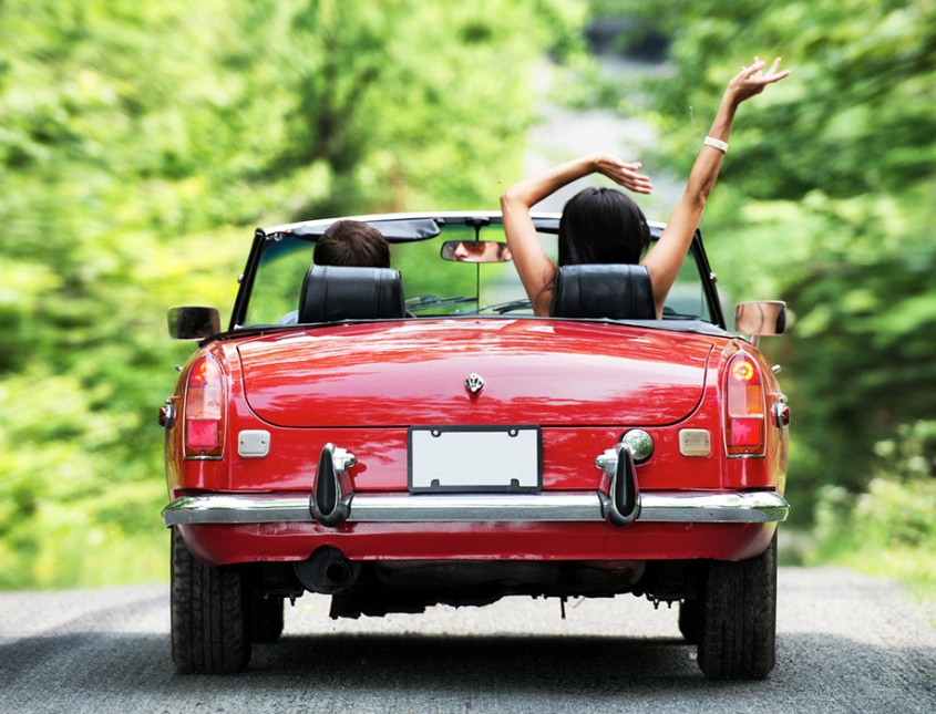 two people driving in the trees in red convertible 