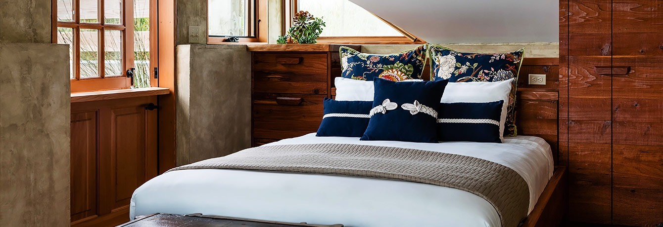 guest room with angled ceilings, white linens with navy throw pillows, and wooden accents close up of bed