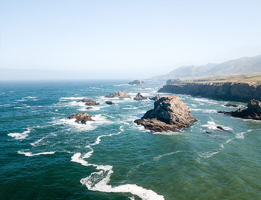 aerial view of the ocean water with large rocks and cliffs