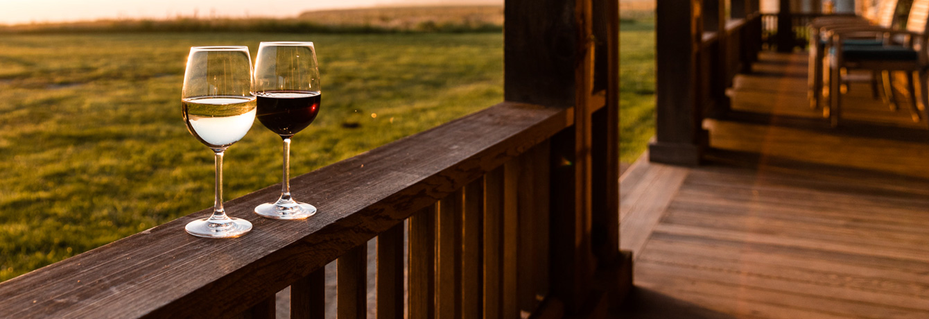 two glasses of wine sitting on a wooden porch railing