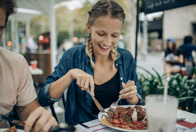 woman cutting food on a plate at an outside restaurant 