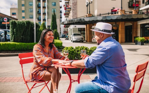 couple sat in a red table drinking wine in a exterior place of the hotel with garden behind them
