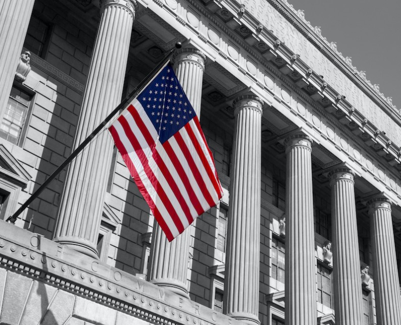 exterior of government building in black and white with american flag hanging off the side in color