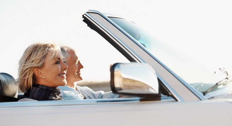 senior couple driving a white convertible car and smiling