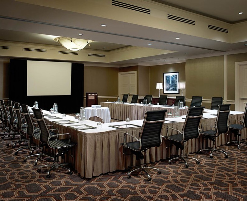 meeting space setup with long tables and executive leather chairs facing a projection screen