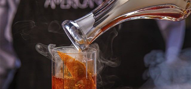 image of bartender pouring smoke into a bourbon drink served in a tall glass
