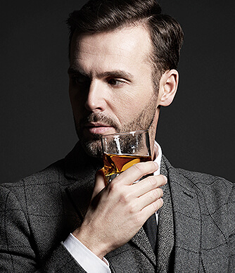 man drinking a glass of bourbon wearing a suit
