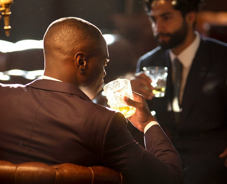 two men in suits drinking cocktails sitting in brown leather chairs