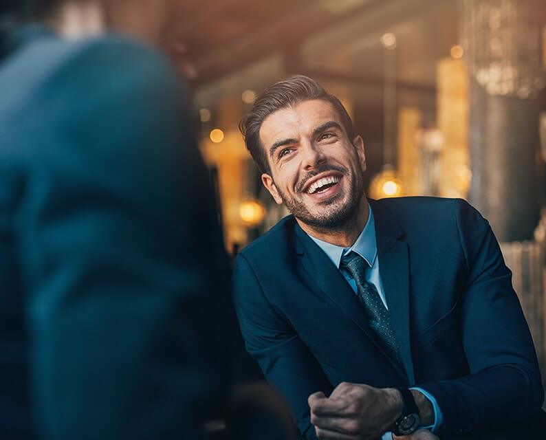 man in blue suit and blue shirt and tie laughing with a collogue