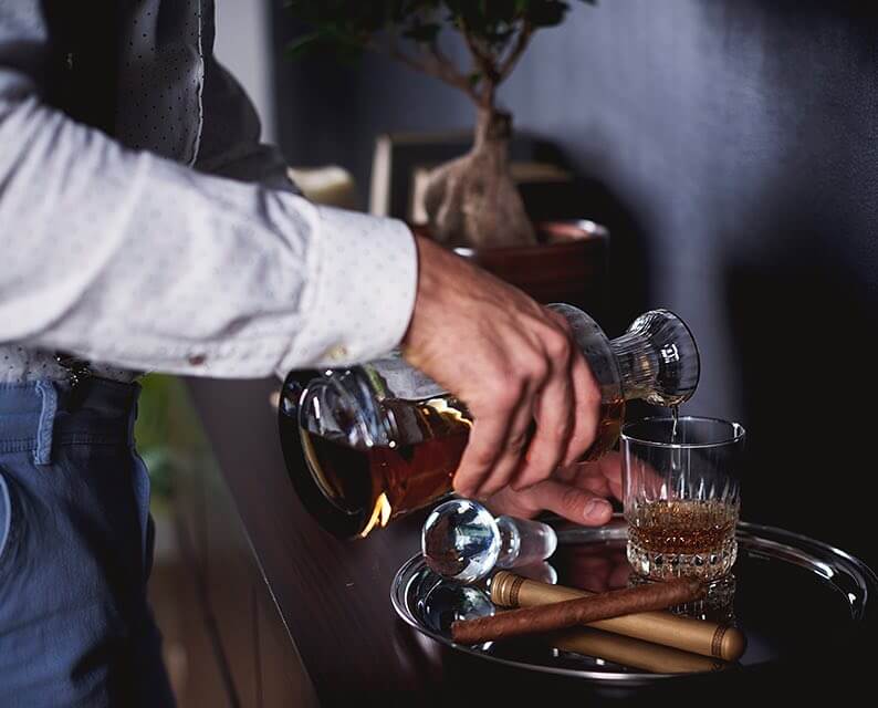 man in white dress shirt pouring a cocktail from a decanter at a bar