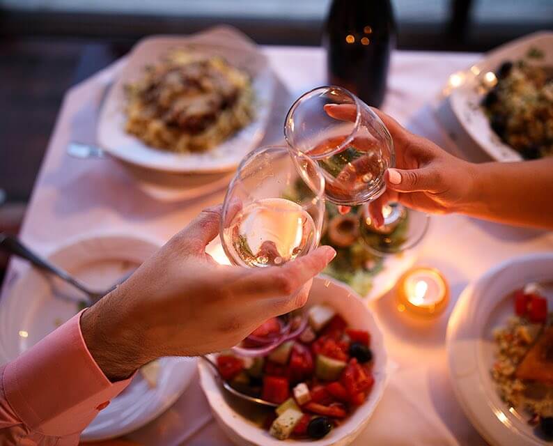 couple toasting wine glasses over a dining table lit by candlelight