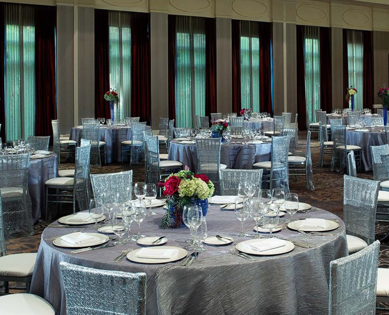 venetian ball room with large round tables and chairs with silver table cloths and white place-settings