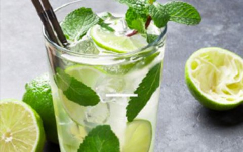 a refreshing mojito in a glass cup with mint and limes next to it for an artsy effect