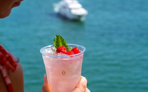 a boat in the background while a lady is holding a drink