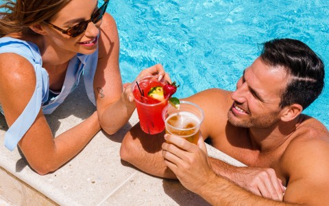 woman and man clinking tropical drinks by the pool