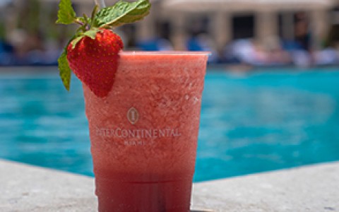a strawberry frozen drink with a fresh strawberry as decoration, it is on the edge of the pool on a sunny day