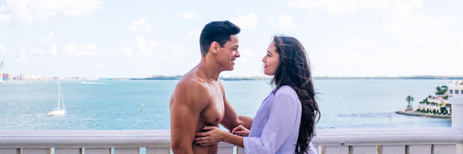 a couple smiling at each other while the miami bay is behind them