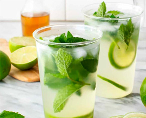 Two cups of mojitos garnished with basil and limes