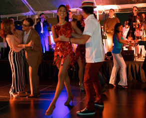 People dancing salsa, main focus is a girl wearing a red dress dancing with man in a white shirt and straw hat