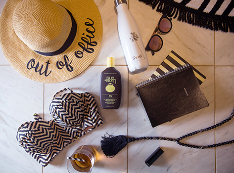 A flat lay image of travel accessories, sunglasses, sunscreen, hat