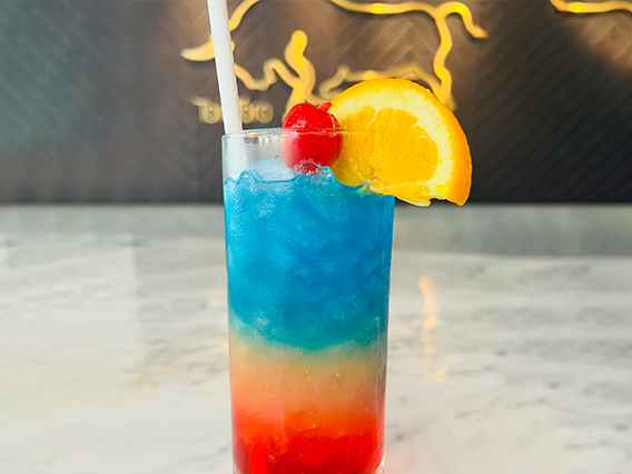 image of toro toro's "love is love" cocktail - blue and red colored drink in tall glass garnished with a cherry and orange slice