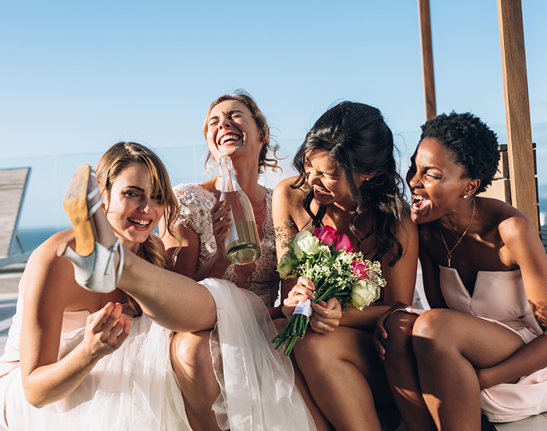 A bride and her bridal party laughing together sitting outside