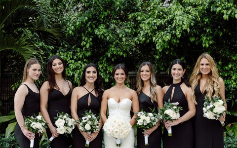 A smiling bride and her bridesmaids standing in front of tropical trees.