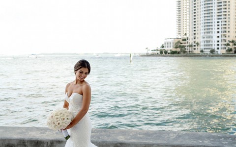 A bride holding a white flower bouquet next to the water during the day.