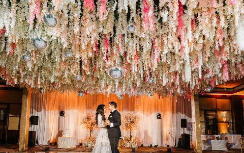 A husband and wife dancing on a white dance floor under disco balls and flowers hanging from the ceiling.