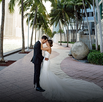 A bride and groom hugging and looking at each other underneath the palm trees.