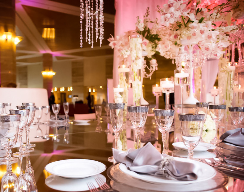 A table setup for dinner with white and pink flowers, candles, and crystals hanging down from the ceiling.