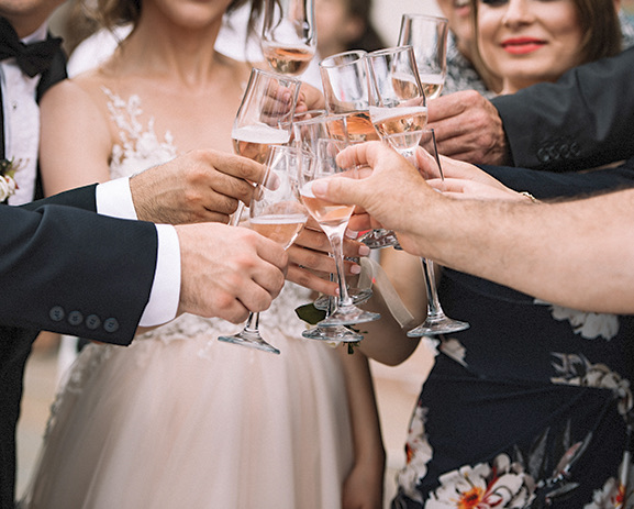 A group of guests at a wedding clinking champagne glasses and smiling.