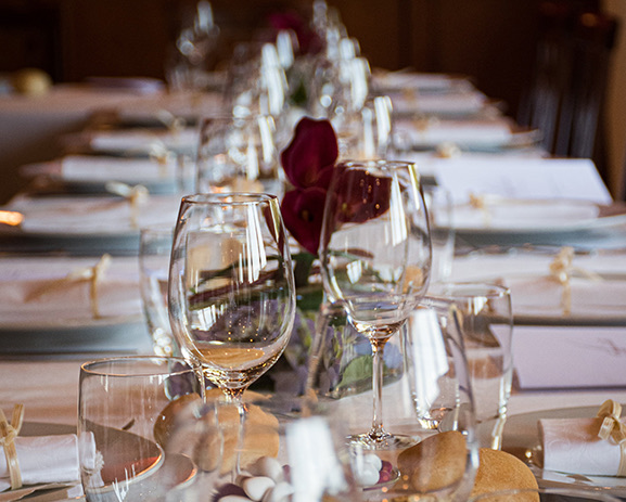 A long table setup for dinner with white linens and red flowers.
