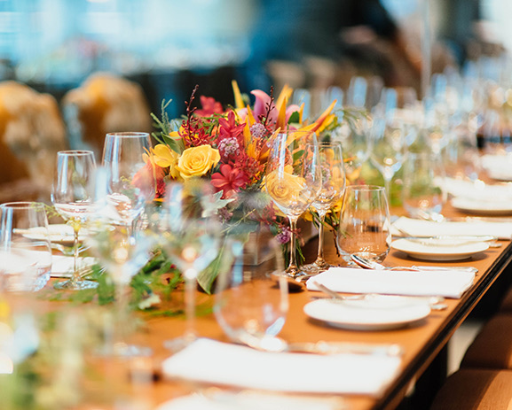 A long table setup for dinner with wine glasses and colorful floral centerpieces.