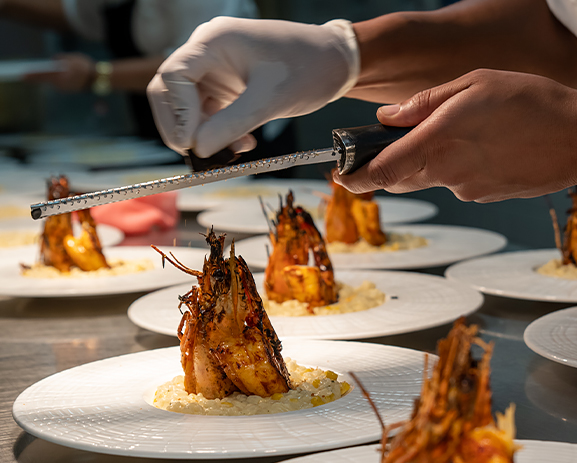 A chef grinding a fresh spice over prepared lobster.
