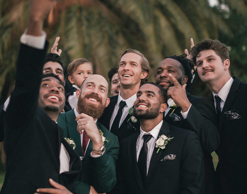 A group of smiling men taking a picture with palm trees behind.