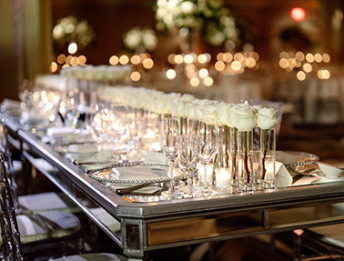 A long table setup for dinner with multiple white roses in vases as the centerpieces.