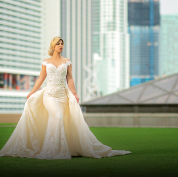 A bride wearing a dress off the shoulders and walking in the lawn while looking off to the side.