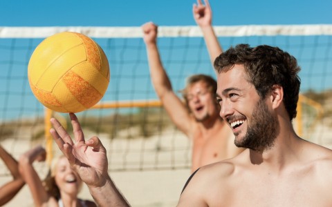 Man playing with volleyball with friends cheering in the back 