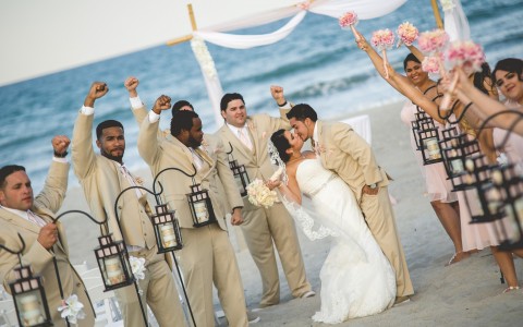 Bride and groom kissing in between bridesmaids and groomsmen on the beach  