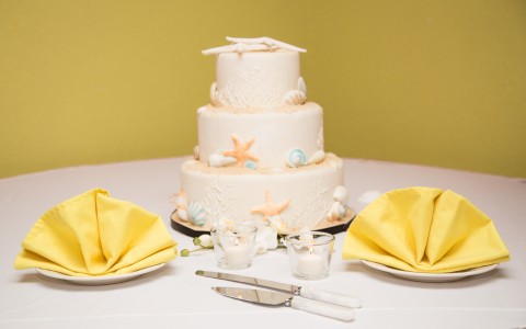 Wedding cake with sugar seashell decor next to yellow napkins in the shape of shells 