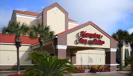 front view of a hotel called hampton inn & suite with palmas and flowers