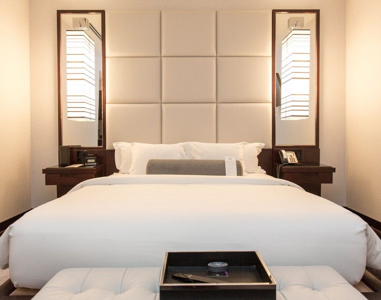 A room with a large white bed and a black tray with bright lighting. 