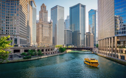 A waterway with a large yellow boat in it and tall buildings to the left and to the right.