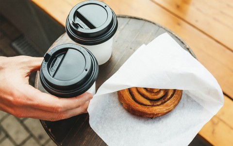 Two coffees and a cinnamon roll on a small wooden round table.