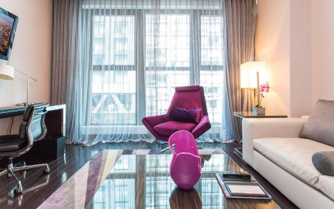 A room with sheer gray curtains and a bright purple velvet chair.